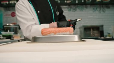 Suşi restoranında servis etmeden önce elinde gaz ocağıyla somon sarması kızartan suşi şefinin yakın çekimi.