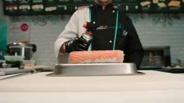 Suşi restoranında servis etmeden önce elinde gaz ocağıyla somon sarması kızartan suşi şefinin yakın çekimi.