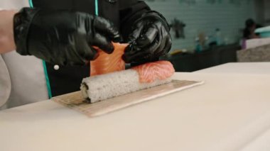 Bir suşi şefi, bambu hasırının üzerinde karides ve chuka yosunuyla lezzetli bir rulo hazırlar.