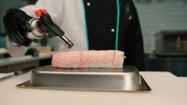 Suşi restoranında servis etmeden önce elinde gaz ocağıyla somon sarması kızartan suşi şefinin yakın çekimi.