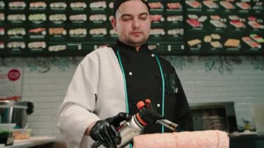 Suşi restoranında servis etmeden önce elinde gaz ocağıyla somon sarması kızartan suşi şefinin yakın çekimi.