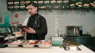Elinde tabletle dalgın bir suşi şefi lezzetli böreklerin tariflerine bakar ve malzemelerini seçer.