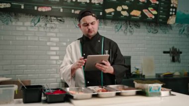 Elinde tabletle dalgın bir suşi şefi lezzetli böreklerin tariflerine bakar ve malzemelerini seçer.