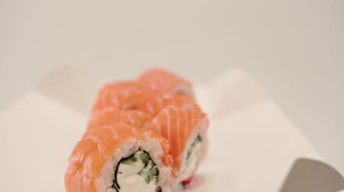 Suşi kutusunda beyaz bir arka planda salatalık ve süzme peynirli Philladelphia dürümünün yakın çekimi.