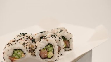 Salatalık mango pilavı ve beyaz arka planda susam olan somonlu bir rulo yakın çekim.