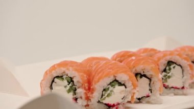 Suşi kutusunda beyaz bir arka planda salatalık ve süzme peynirli Philladelphia dürümünün yakın çekimi.