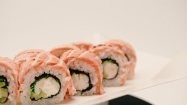 Kurutulmuş somon, salatalık ve peynirli bir rulo yakın plan suşi teslimat kutusunda beyaz arka planda.