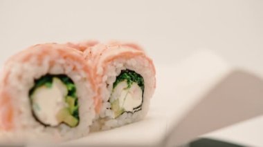 Kurutulmuş somon, salatalık ve peynirli bir rulo yakın plan suşi teslimat kutusunda beyaz arka planda.