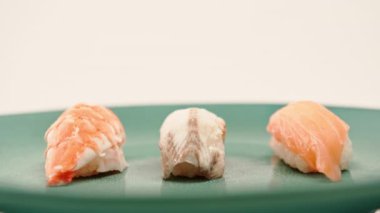 Beyaz arka planda mavi bir tabakta duran yılan balığı ve karidesli üç nigiri suşisi.
