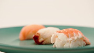 Beyaz arka planda mavi bir tabakta duran yılan balığı ve karidesli üç nigiri suşisi.