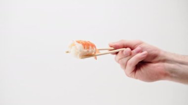 Beyaz arka planda karides sushi nigiri tutan bir adamın ellerinin yakın çekimi.