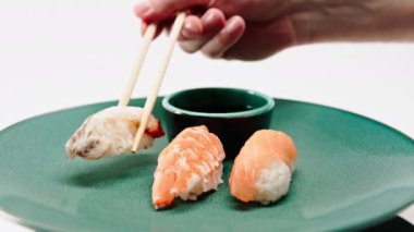 Yemek çubuklarıyla soya sosuna karides suşisi ve somon tabağından yılan balığı suşisi alıp batırmak için yakın plan.