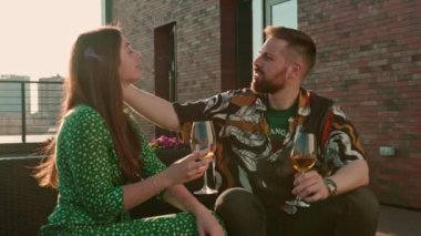 Genç bir çift, ellerinde kadehlerle ellerinde şarapla terasta oturmuş suşi yiyorlar ve sohbet ediyorlar.