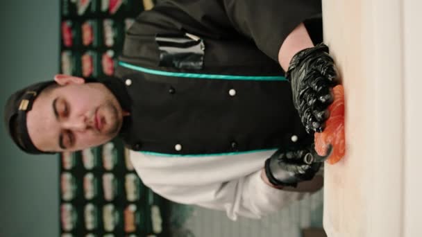 Pystysuora Video Lähikuva Sushi Kokki Leikkaamalla Lohifilee Veitsellä Valmistellessaan Sushia — kuvapankkivideo