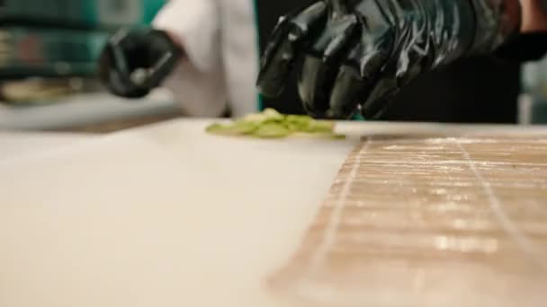 Крупный План Производителя Суши Перчатках Режущего Авокадо Профессиональным Кухонным Ножом — стоковое видео