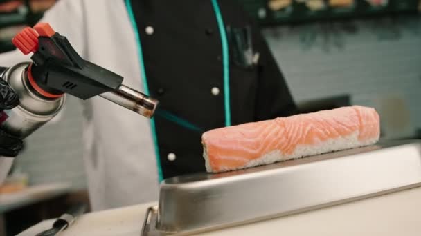 寿司屋で召し上がる前に 手揚げサーモンロールのガスバーナーと寿司シェフのクローズアップ — ストック動画