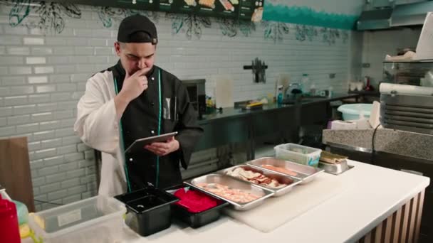 Zamyślony Kucharz Sushi Tabletem Rękach Patrzy Przepisy Pyszne Bułki Wybiera — Wideo stockowe
