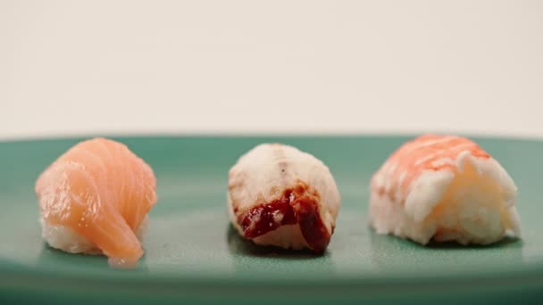 三个黑鱼寿司与鳗鱼和虾仁的特写镜头躺在一个白色背景的蓝色漂亮盘子上 — 图库视频影像