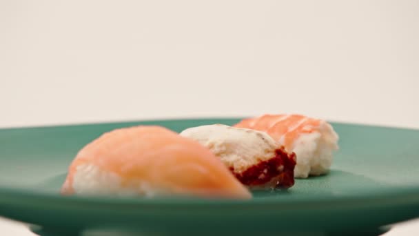 白い背景に青い美しいプレートの上にウナギサーモンとエビが横たわった3匹のニギリ寿司のクローズアップ — ストック動画