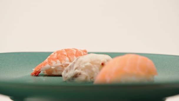 三个黑鱼寿司与鳗鱼和虾仁的特写镜头躺在一个白色背景的蓝色漂亮盘子上 — 图库视频影像