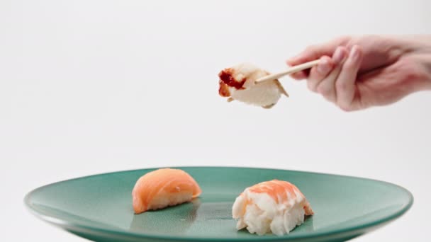 一只雄性手的特写镜头 用筷子从白底鲑鱼和虾寿司盘中取出一条鳗鱼寿司 — 图库视频影像