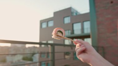 Adamın yemek çubuklarıyla çekilmiş yakın çekimi. Bir yaz terasında nefis bir suşi rulosu. Gökyüzünün arka planında.