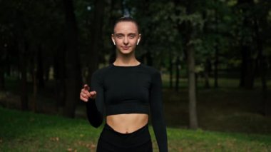 Profesyonel bir atlet kızın portresi parkın arka planına karşı bir jestle nasıl egzersiz yapılmayacağını gösteriyor.