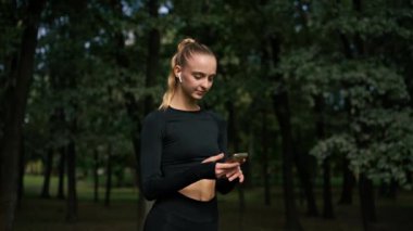 Spor kıyafetli bir kız dikkatlice bakıyor ve parkta telefonla konuşuyor. İnternetten antrenman yapmayı seçiyor.