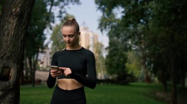 Spor kıyafetli bir kız dikkatlice bakıyor ve parkta telefonla konuşuyor. İnternetten antrenman yapmayı seçiyor.
