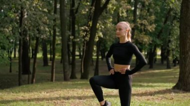 Sabah sporu yapan bir kız temiz havada egzersiz yaparken bacağı kalçasını esnetirken dairesel hareketler yapıyor.