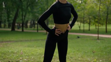 Spor üniformalı bir kız sporcu Park 'taki antrenmandan önce ısınma sırasında boyun ve omuz büküyor.