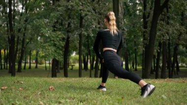 Spor kıyafetli genç bir kız antrenman dengesi kurmak ve bacak kaslarını germek için hareket egzersizi yapıyor.