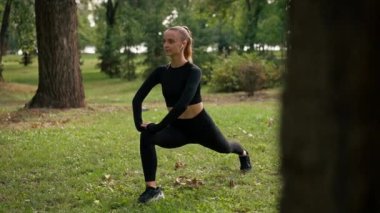 Spor kıyafetli genç bir kız egzersiz yapıyor tren dengesi ve bacak ve bacak kaslarını esnetiyor.