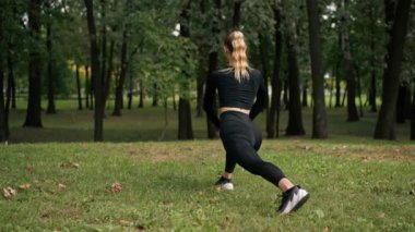 Spor kıyafetli genç bir kız antrenman dengesi kurmak ve bacak kaslarını germek için hareket egzersizi yapıyor.