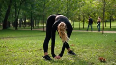 Genç bir bayan sporcu, açık hava spor sahasında esneklik ve sırt sağlığı için ısınma çalışması yapıyor.
