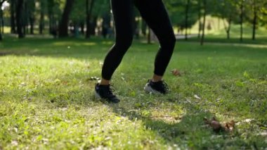 Parkta sabah antrenmanı yaparken yeşil çimlerden atlayan kadın bacaklarının yakın çekimi.