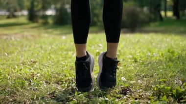 Yeşil çimlerin üzerinde zıplayan kadın bacaklarının yakın çekimi sabah antrenmanı sırasında aktif yaşam tarzı için ısınma egzersizi yapıyor.