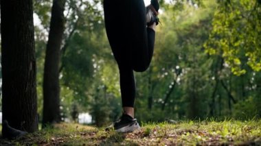Bacaklarını esneten kadın bacaklarının yakın çekimi sabah parkta antrenman yaparken yeşil çimenleri esnetiyor.