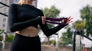 Lastik bantlarla egzersiz yapan bir kızın yakın plan çekimi sokakta çalışırken kol kaslarını güçlendirir.