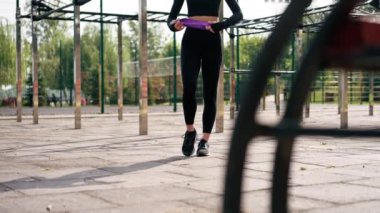 Spor üniformalı güzel bir kız spor sahasında bacaklarını lastik bantla şişirmek için egzersiz yapıyor.