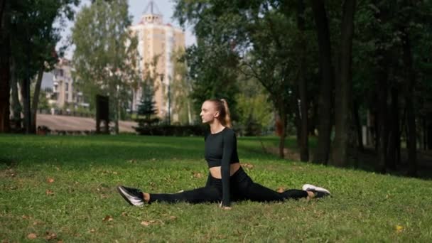 若い美しい女の子がスプリットに座り 公園でのアクティブなライフスタイルで朝のトレーニング後に伸びる — ストック動画