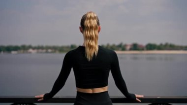 Güzel bir kız sporcu parkta köprüde durup dinlenirken dikiz manzarasının tadını çıkarıyor.