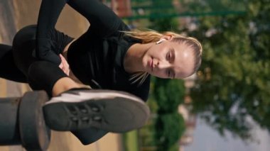 Dikey video portresi genç kız spor eğitmeni yan sırt kaslarını caddedeki yüksek makineye atarak geriyor.