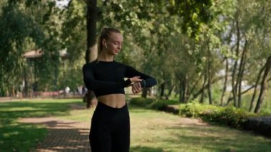 Parkta sabah koşusu yapan sporcu kız, kaç kilometre koştuğunu belirlemek için elindeki spor saatine bakıyor.
