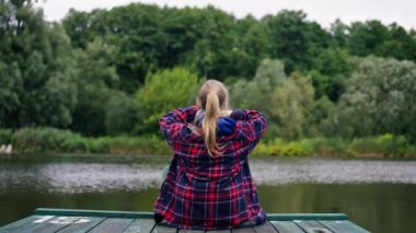 Piers 'daki bir nehir ya da gölün kıyısında oturan bir kızın arkadan görünüşü depresif devlet düşünceleri.