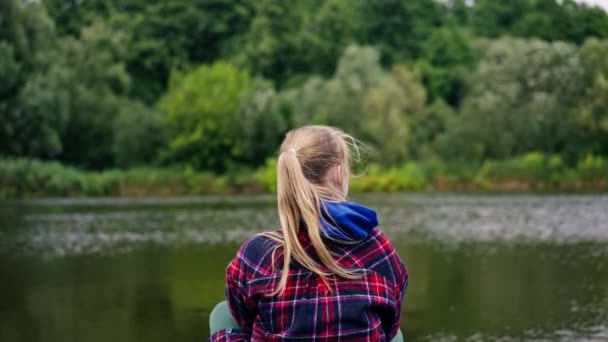 ピアーズの川や湖の岸に座っている女の子のバックビュー 自然抑うつ状態の考え — ストック動画