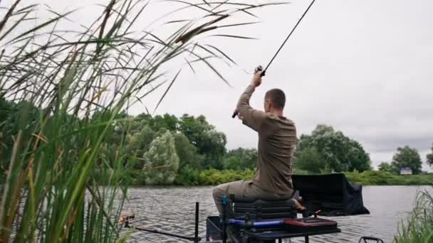 有钓竿或纺纱的渔夫和专业工具坐在河岸后视镜上 把鱼拖出湖中钓鱼 — 图库视频影像
