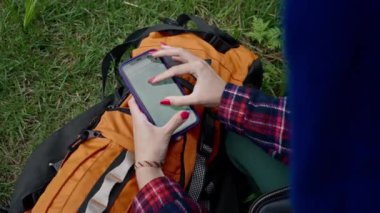 Doğanın arka planında bir turist sırt çantasının yakın çekimi. Elinde akıllı bir telefon ve harita var. Profesyonel ekipman.