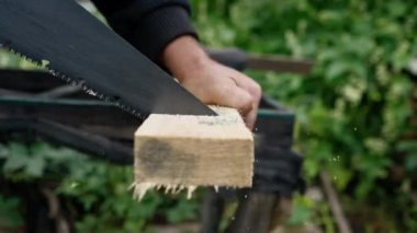Odunun ahşap bir parçasını tutan ve kereste testeresiyle testereyle kesen bir adamın ellerinin yakın çekimi.