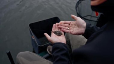 Yakından erkek balıkçının eli, balık yakalamak için oltaya yem takıyor.